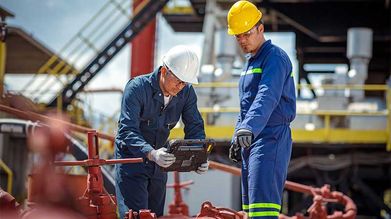 two site operators inspecting pipes on an oil and gas worksite